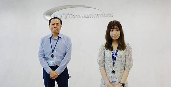 受付デスク背後のロゴの前で