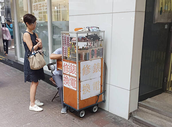 雑居ビルの外にある電池交換の屋台でおじさんが仕事中